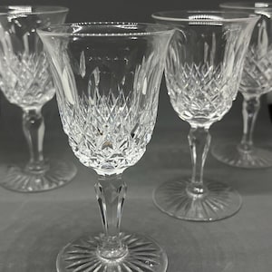 Puede incluir: Un conjunto de cuatro copas de cristal transparente con un patrón de corte de diamante en el cáliz, un tallo facetado y una base circular con un diseño de rayos solares. Las copas están dispuestas en grupo, mostrando su superficie texturizada.