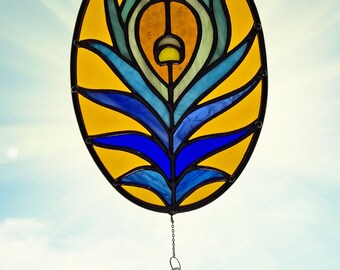 May include: Oval stained glass window panel featuring a peacock feather design. The panel has a yellow background with blue, green, and orange accents. A chain and crystal pendant hang from the bottom. Decorative art for home decor.