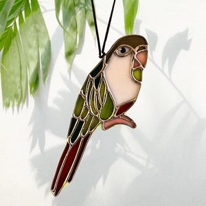 May include: A stained glass parrot ornament with green, red, and white glass pieces. The parrot is hanging from a black string.