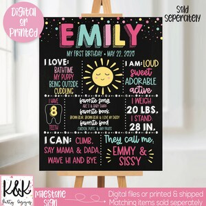 May include: A black chalkboard style sign with a pink, blue, and yellow design. The sign says "Emily" and includes details about her first birthday, including her weight, height, favorite foods, and activities. The sign also includes a sun graphic and a tooth graphic.