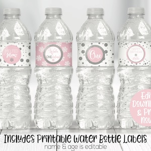 Peut inclure: Quatre bouteilles d'eau en plastique transparent avec des &eacute;tiquettes de flocons de neige et de pois rose et argent. Les &eacute;tiquettes indiquent "Melted Snow", "Winter One", "One" et "Happy Birthday Addie". Le texte "Edit, Download & Print now!" est sur un cercle rose. Le texte "Includes Printable Water Bottle Labels name & age is editable" est sous les bouteilles.