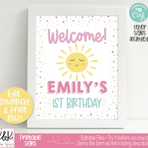 May include: A printable welcome sign for a first birthday party. The sign features a yellow sun with a pink face and the text "Welcome! Emily's 1st Birthday" in pink and blue.