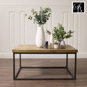 May include: A wooden coffee table with a black metal frame. The table is decorated with two vases, one with green plants and the other with white flowers, and two candles.