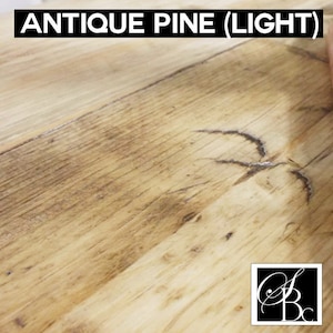 May include: Close-up of a light wood surface with a knot in the wood. The wood has a light brown color with a slightly reddish hue. The surface is smooth and has a slight sheen. The wood is called "Antique Pine (Light)".