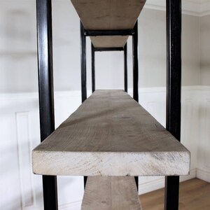 May include: A close-up of a wooden shelf unit with black metal supports. The shelf is made of reclaimed wood and has a rustic look.