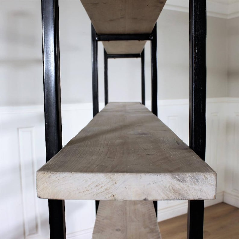 May include: A close-up of a wooden shelf unit with black metal supports. The shelf is made of reclaimed wood and has a rustic look.