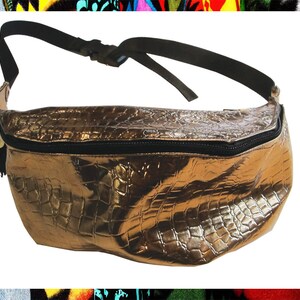 Pode incluir: Uma pochete dourada met&aacute;lica com um design em relevo de crocodilo. A bolsa tem uma al&ccedil;a ajust&aacute;vel preta e um z&iacute;per preto.