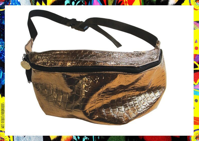 Pode incluir: Uma pochete dourada met&aacute;lica com um design em relevo de crocodilo. A bolsa tem uma al&ccedil;a ajust&aacute;vel preta e um z&iacute;per preto.