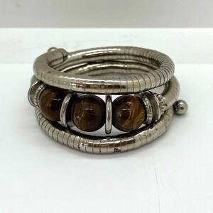Pode incluir: Um bracelete de prata com contas de olho de tigre castanho. O bracelete é feito de várias voltas de corrente de prata e tem um design flexível.