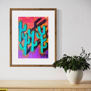 Pode incluir: Uma pintura abstrata emoldurada de cactos em tons turquesa, rosa, roxo e preto com a palavra "TIPH" escrita em preto na parte inferior.