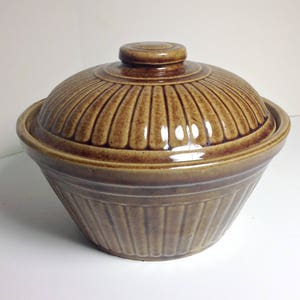 May include: A brown ceramic casserole dish with a lid. The dish has a fluted design and a glossy finish.