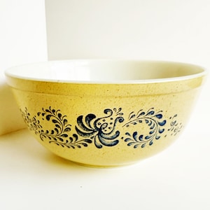 May include: A yellow ceramic mixing bowl with a white interior. The exterior features a speckled texture and is decorated with a blue floral pattern. The bowl is ideal for kitchen use.