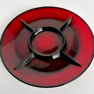 May include: A red glass serving dish with four sections. The dish has a diamond pattern and a raised center section.