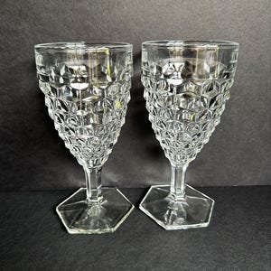 May include: Two clear, vintage-style wine glasses. Each glass features a textured, geometric pattern on the bowl and a hexagonal base. The stems are slender and the glasses are made of clear glass.