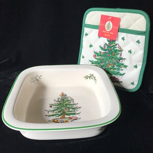 May include: A square ceramic baking dish with a cream-colored interior featuring a decorated Christmas tree and green rim, paired with a matching quilted fabric pot holder that displays a Christmas tree and a red Spode brand tag.