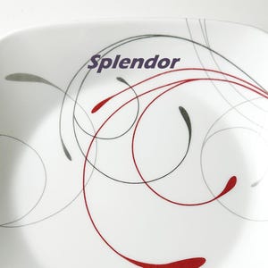 May include: White square plate with a decorative design. The plate features a swirling pattern of red, gray, and black lines. The word "Splendor" is printed in purple on the plate.