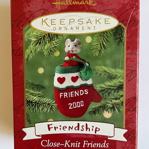 May include: Red and green Hallmark Keepsake Ornament featuring a white mouse peeking out of a red knitted mitten with white hearts and the text "Friends 2000". The ornament is part of the "Friendship Close-Knit Friends" collection and is one of two ornaments.