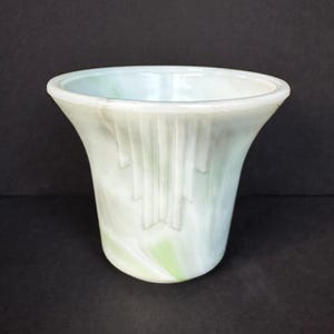 May include: A white and green glass vase with a fluted design. The vase has a wide mouth and a narrow base.