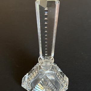 May include: A clear glass perfume bottle with a geometric design. The bottle has a tall, pointed stopper and a star-shaped base.