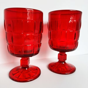 May include: Two red glass goblets with a square patterned design. The goblets have a short stem and a wide base.