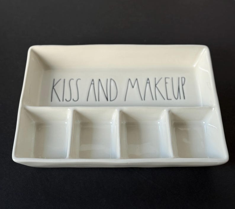 May include: A rectangular off-white ceramic tray with a glossy finish, featuring four distinct compartments. The upper section is a wide, open space with the black text KISS AND MAKEUP printed in a simple, hand-lettered style font.