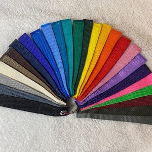 May include: A fan of colorful fabric swatches in various shades, including black, gray, beige, blue, green, yellow, orange, red, pink, and purple. The swatches are attached to a metal ring, showcasing a wide range of color options.