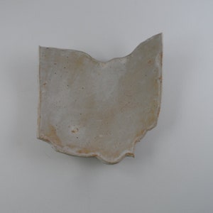 May include: A ceramic dish shaped like the state of Ohio. The dish is a light gray color with a slightly rough texture.