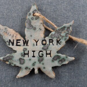 May include: A ceramic leaf ornament with a green and white glaze and black speckles. The leaf has a string attached and the words "NEW YORK HIGH" are written on the front.
