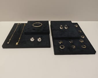 May include: Jewelry display featuring gold necklaces, bracelets, earrings, and rings. The jewelry is arranged on black velvet display blocks. The earrings include pearl and gemstone designs. The rings vary in style, including bands and gemstone settings.