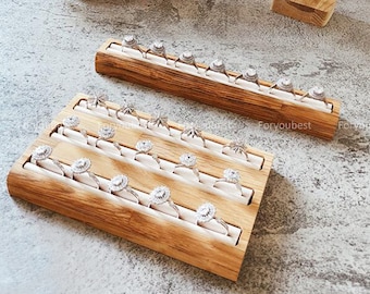 May include: Wooden ring display with multiple rows of slots for rings. The display is made of light brown wood and has a natural finish. The rings are not included.
