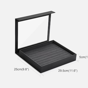Puede incluir: Caja de anillos negra con tapa transparente e interior de terciopelo gris. La caja mide 29,5 cm por 25 cm por 5 cm.