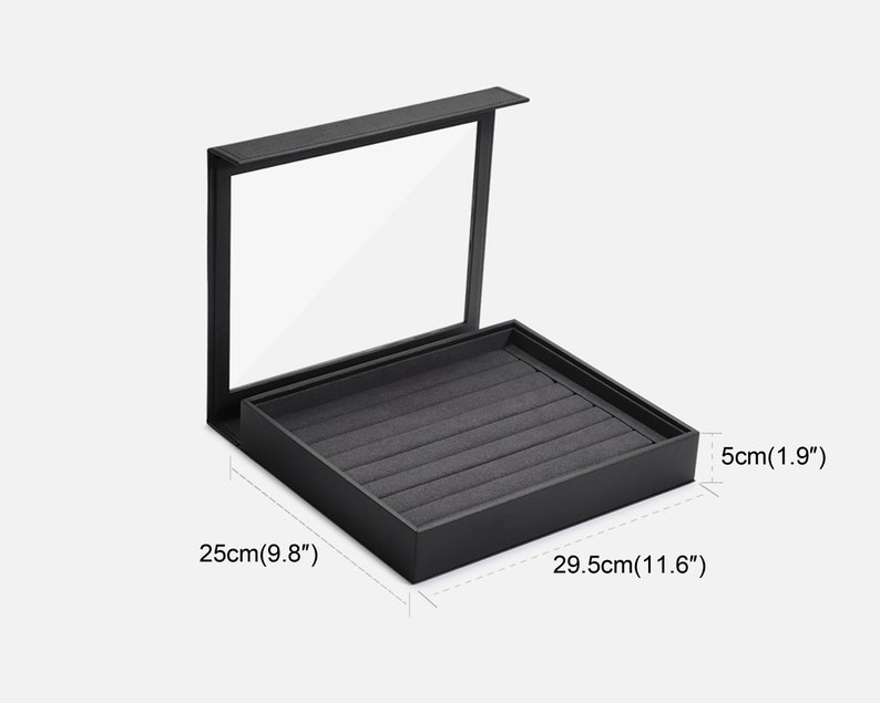 Puede incluir: Caja de anillos negra con tapa transparente e interior de terciopelo gris. La caja mide 29,5 cm por 25 cm por 5 cm.