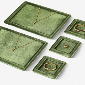 May include: An assortment of jewelry displayed on olive green velvet trays. The jewelry includes gold necklaces, bracelets, and a ring. The trays are rectangular and square, creating an organized presentation. The jewelry is set against a white background.