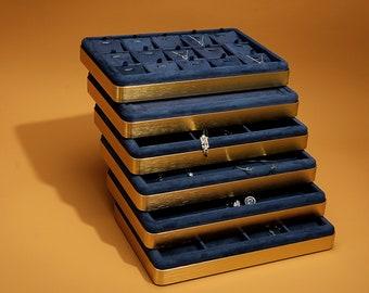 May include: A stackable jewelry organizer with six tiers, each lined with blue velvet and trimmed with a gold band. The organizer is filled with various jewelry pieces, including necklaces, earrings, and rings.