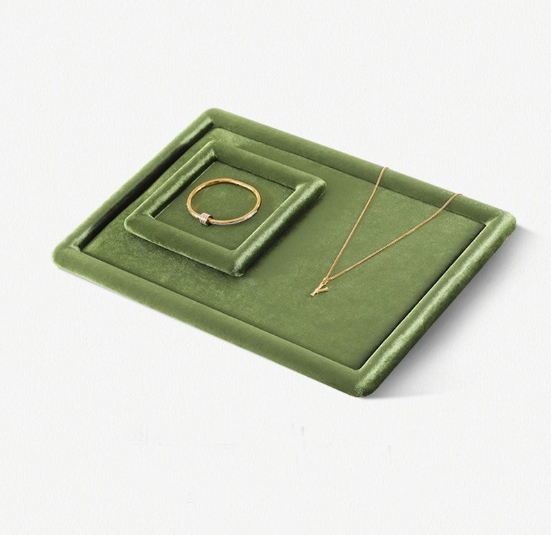 May include: Olive green velvet jewelry display trays. A gold bracelet with a diamond accent sits in the smaller tray. A gold necklace with a pendant rests on the larger tray. The trays are square with rounded corners.