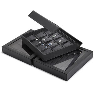 Puede incluir: Caja de joyer&iacute;a de cuero negro con tapa transparente. La caja tiene varios compartimentos para guardar pendientes, collares y anillos. La caja est&aacute; abierta y los compartimentos est&aacute;n llenos de joyas.