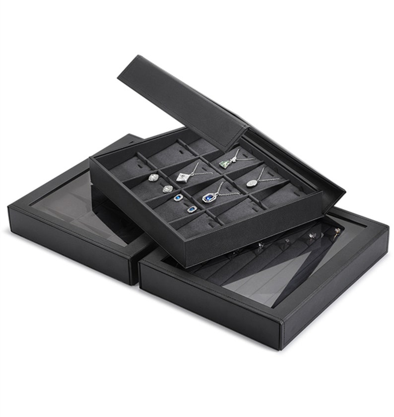 Puede incluir: Caja de joyer&iacute;a de cuero negro con tapa transparente. La caja tiene varios compartimentos para guardar pendientes, collares y anillos. La caja est&aacute; abierta y los compartimentos est&aacute;n llenos de joyas.