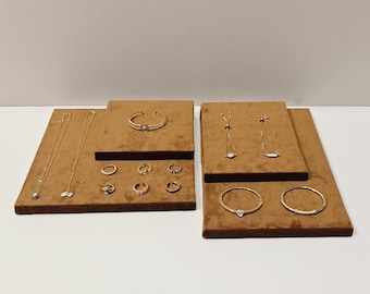 May include: A set of brown velvet jewelry display stands with gold necklaces, bracelets, and rings. The stands are arranged in a rectangular shape on a white surface.