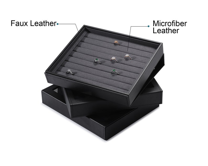 Puede incluir: Bandeja de exhibici&oacute;n de anillos de cuero sint&eacute;tico negro con forro de cuero de microfibra. La bandeja tiene m&uacute;ltiples ranuras para anillos y est&aacute; apilada sobre otras dos bandejas similares.