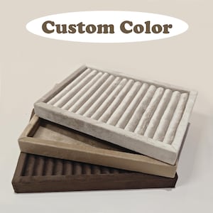 May include: Three stacked jewellery trays in beige, tan, and brown. Each tray has a rectangular shape with a soft, velvety texture and vertical slots for organising jewellery. The top tray is a light beige colour, the middle tray is tan, and the bottom tray is brown. The text "Custom Color" is above the trays.