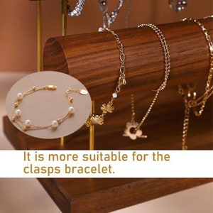 May include: A gold bracelet with pearls and small gold beads is displayed on a wooden jewellery stand. The stand has a dark brown finish and is holding several gold necklaces and bracelets. The text in the image reads: "It is more suitable for the clasps bracelet."