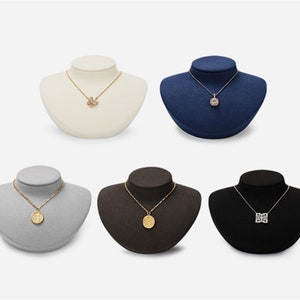 May include: Six necklace display stands with different colored velvet bases. The stands are all the same shape and size. Each stand has a necklace with a different pendant on it. The pendants are a flower, a round stone, a round stone, a square stone, and a star.