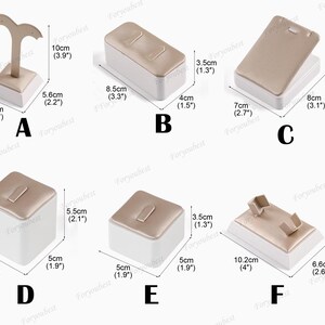 May include: Six different display stands for jewelry, made of white and gold material. The stands are in various shapes and sizes, with some featuring a velvet-like lining. The stands are labeled with letters A through F and have measurements in inches and centimeters.