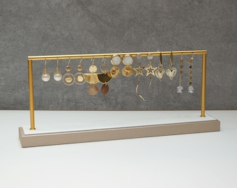 May include: A gold earring display stand with a variety of gold earrings, including stars, hearts, and geometric shapes. The stand is made of metal and has a light brown base.