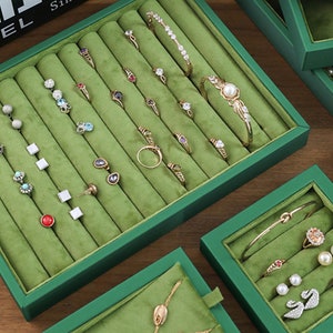 May include: Green velvet-lined jewellery box with multiple compartments for storing rings, earrings, and bracelets. The box has a sleek, modern design and is perfect for organising and displaying your favourite pieces.