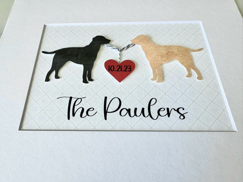 May include: A framed print with two black and brown dog silhouettes holding a red heart with the date 10.21.23. The text "The Paulers" is below the dogs.