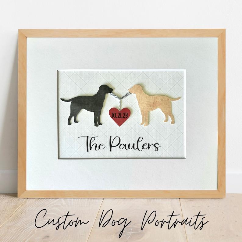 May include: A framed custom dog portrait with two black silhouettes of dogs, a black lab and a yellow lab, connected by a red heart with the date 10.21.23. The text "The Paulers" is below the heart.