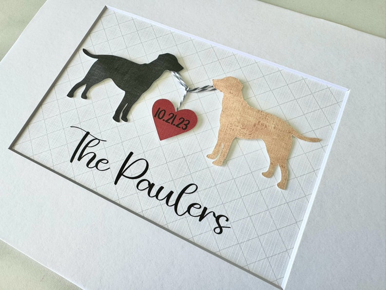May include: A framed print with two black and tan dog silhouettes connected by a red heart with the date 10.21.23 and the text "The Paulers" below.