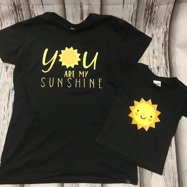 May include: Two black t-shirts with a yellow sun graphic. The larger shirt says "You are my sunshine".