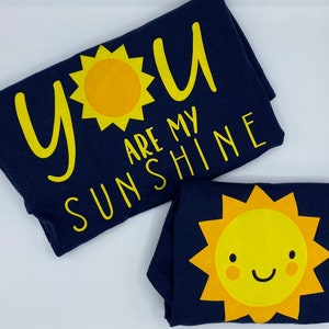 May include: Two navy blue t-shirts with yellow sun designs and the text "You are my sunshine".